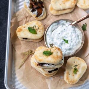 mini naan sliders topped with mint leaves arranged on a baking sheet