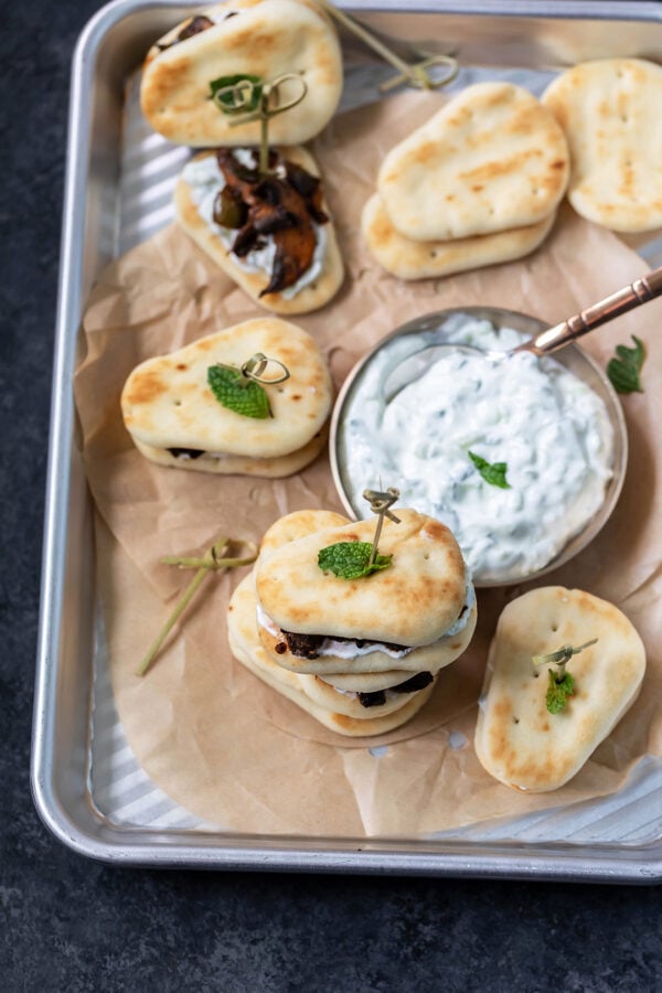 mini naan sliders topped with mint leaves arranged on a baking sheet