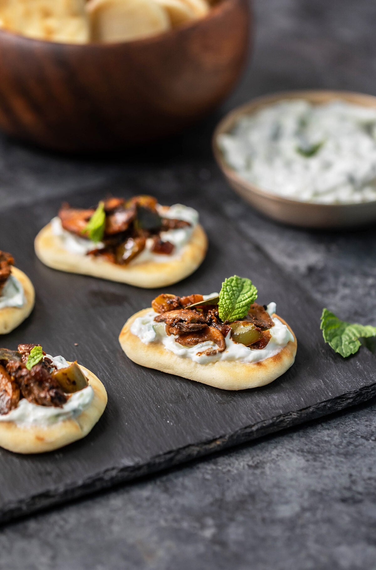 mini naans topped with mushroom filling arranged on a black board