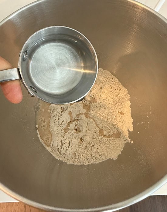 water being added to flour in a bowl