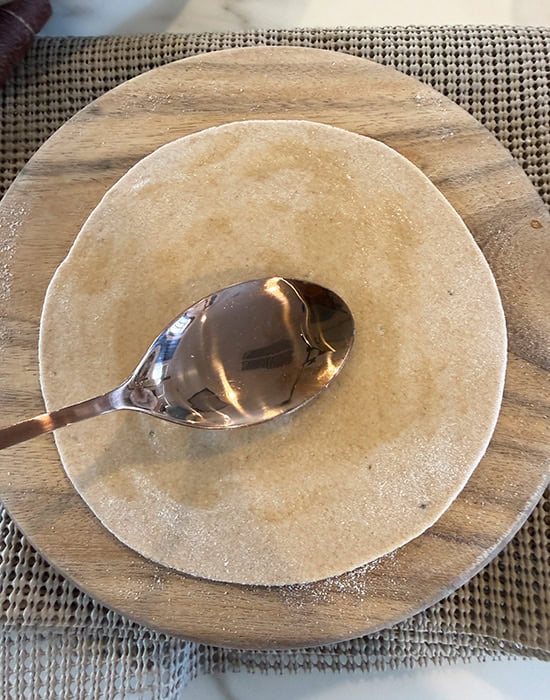 applying oil with a spoon on top of rolled dough