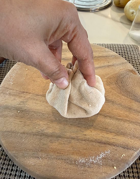 hand pinching sides of the dough to seal the paratha