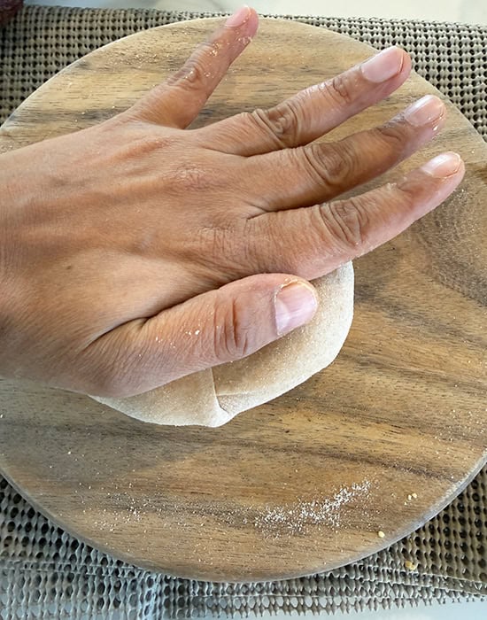 hand pressing a rolled dough to flatten it