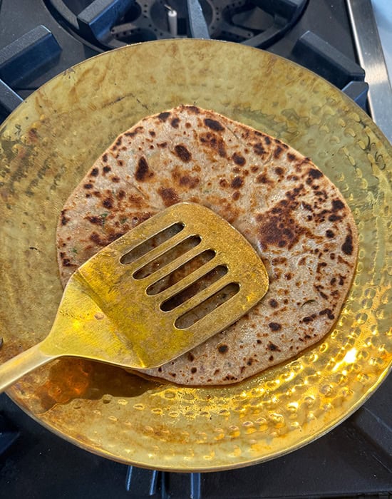 spatula pressing sides of the paratha on a tawa