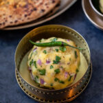 aloo chokha served in a small copper bowl with a green chili placed on top