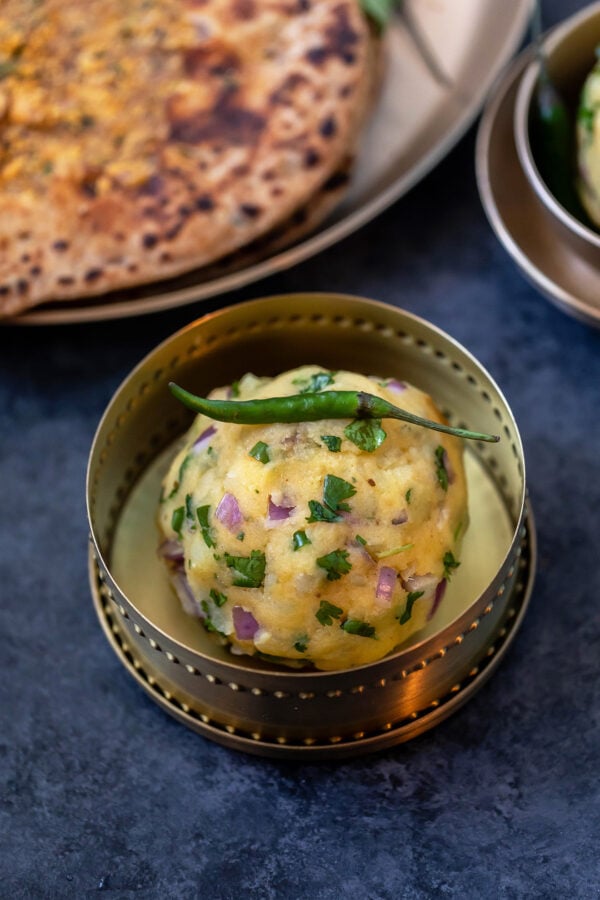 aloo chokha served in a small copper bowl with a green chili placed on top