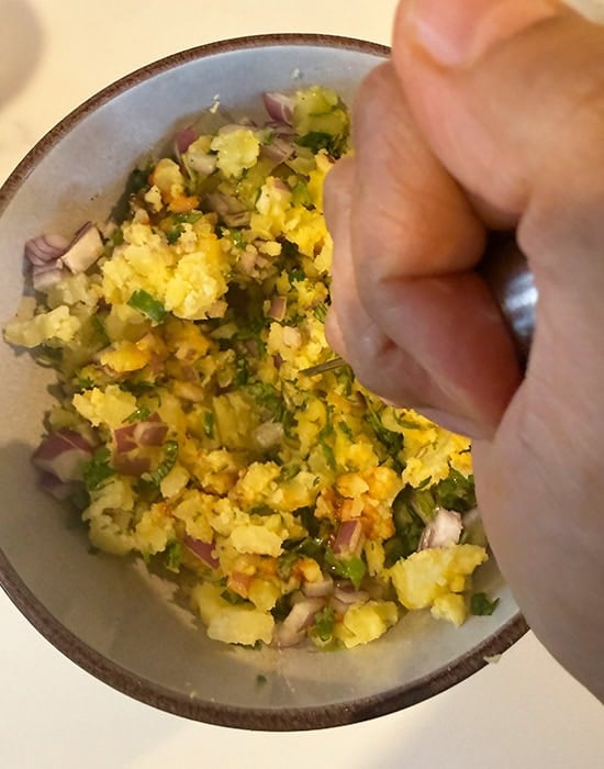 potato masher mashing all the ingredients for aloo chokha in a bowl
