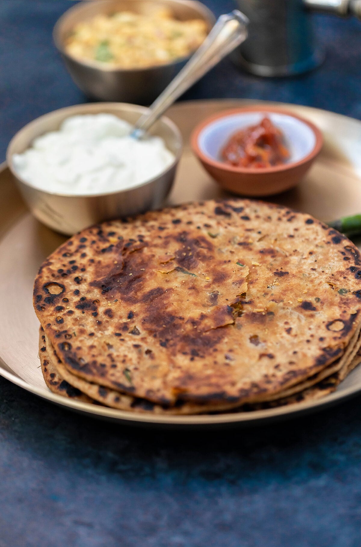 sattu parathas in a brass plate with achar and dahi in the background