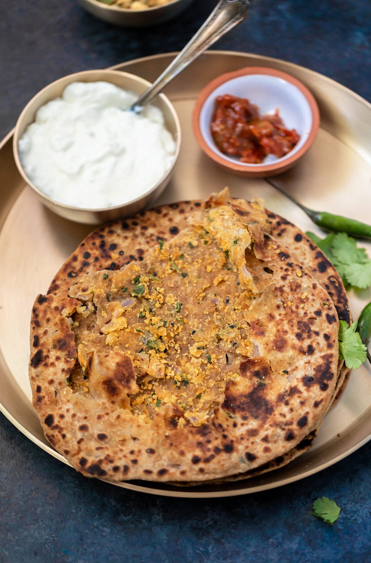 stack of sattu paratha in a plate with bowl of yogurt and achar in the background