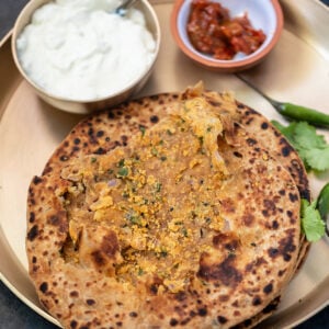 stack of sattu paratha in a plate with bowl of yogurt and achar in the background