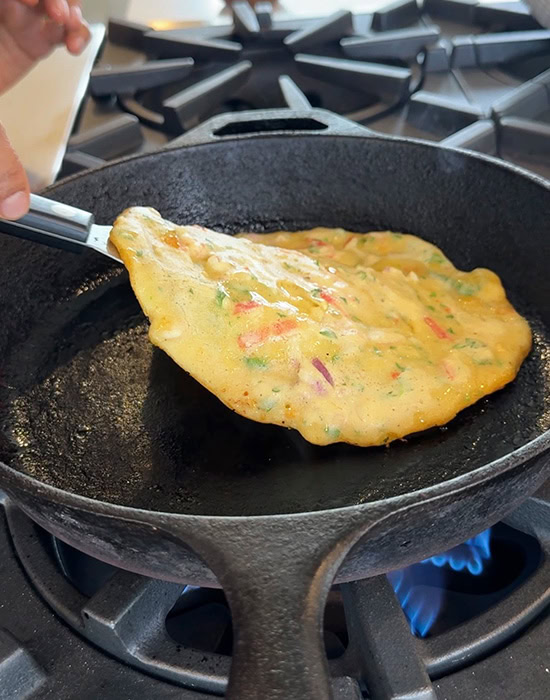 chilla being flipped on an iron pan with help of a spatula