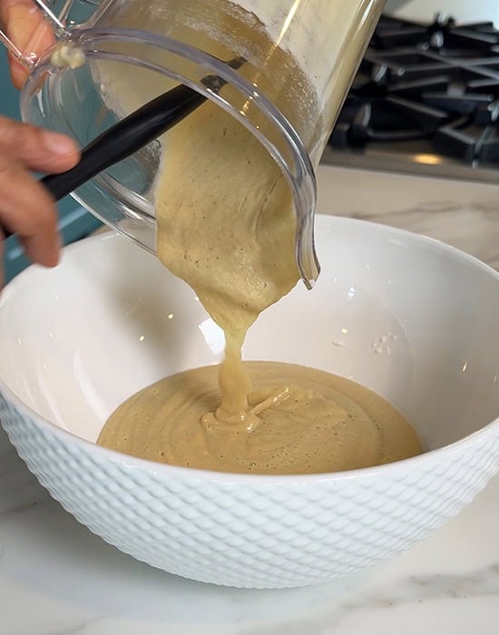 dal batter being poured into a white bowl from a blender