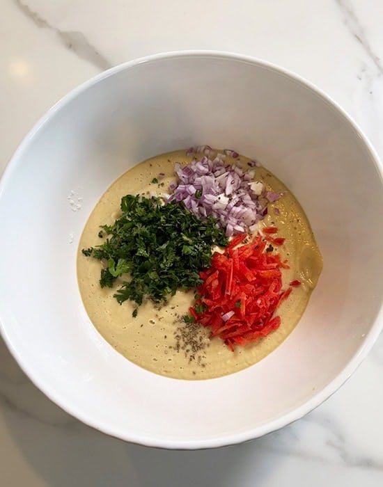 white bowl with dal batter and chopped veggies added to it