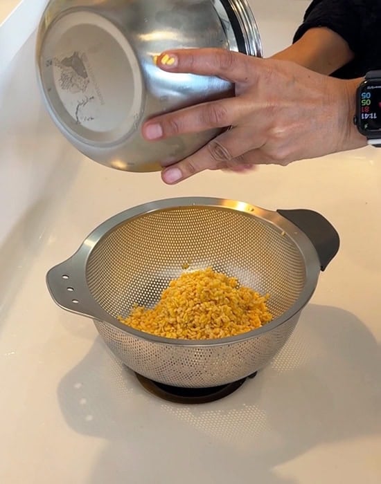 a hand straining soaked dal using a strainer