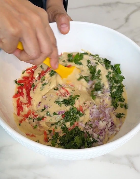 hand mixing dal batter with veggies with a spatula