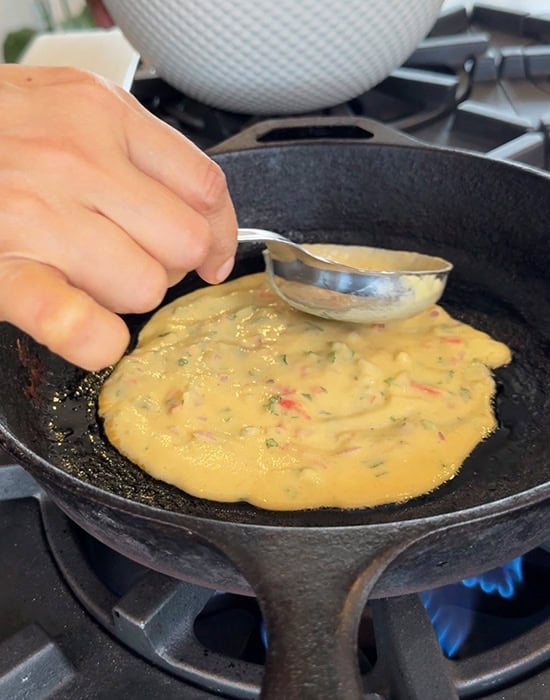 hand spreading dal chilla on a pan with a spatula