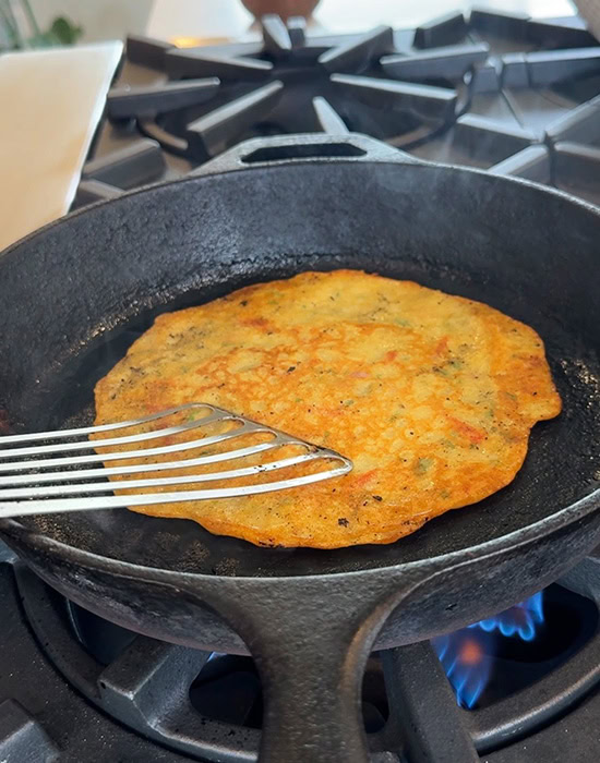 spatula pressing a moong dal chilla on a pan