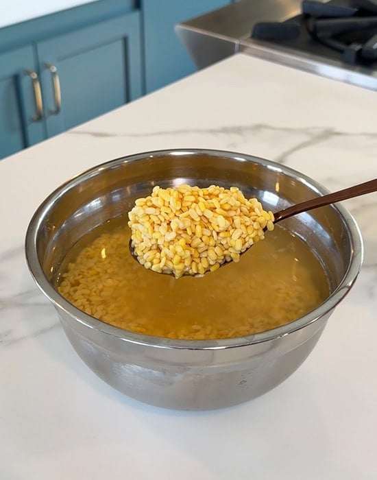 a metal spoon showing soaked dal in a bowl