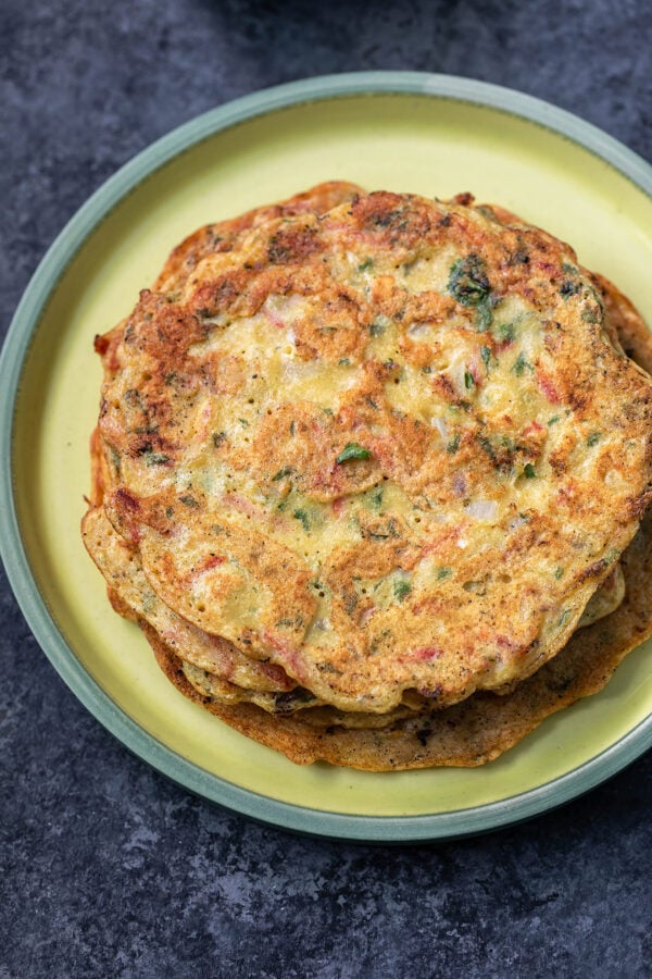 stack of moong dal chillas placed on a yellow color round plate with green rim