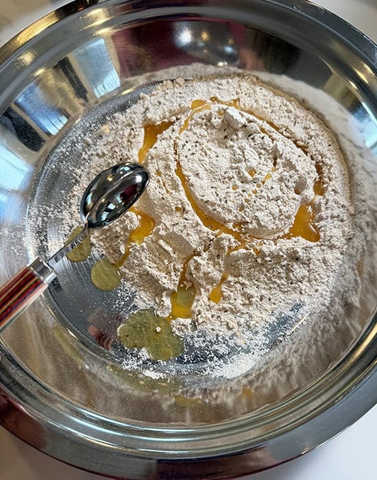 spoon adding oil to flour in a big steel plate