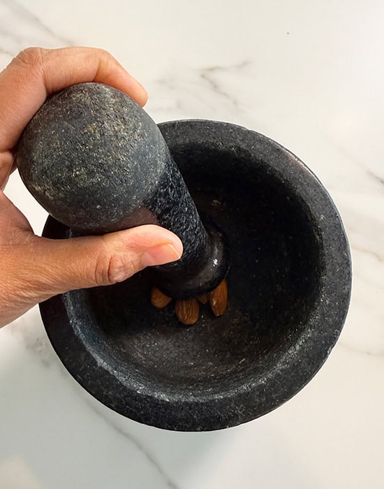 hand using mortar pestle to crush almonds