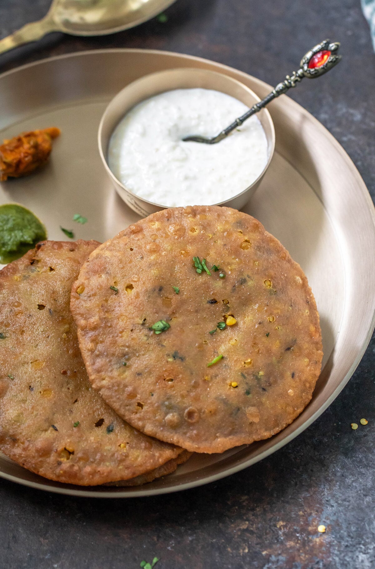 two puris placed on a brass plate with bowl of kheer, chutney and achar