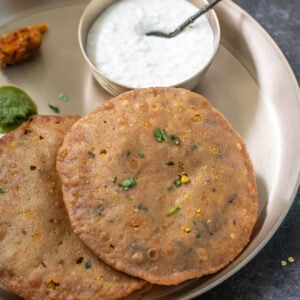 two puris placed on a brass plate with bowl of kheer, chutney and achar