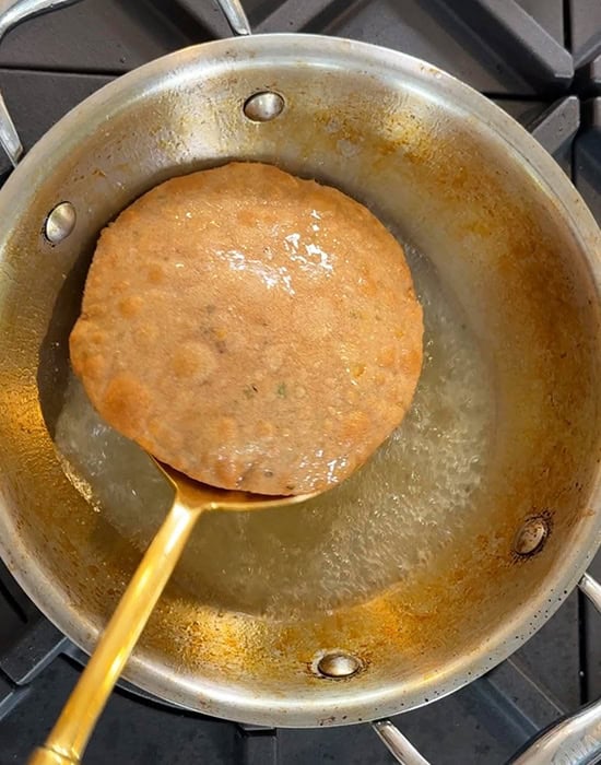 deep fried puri being taken out of hot oil with a spatula