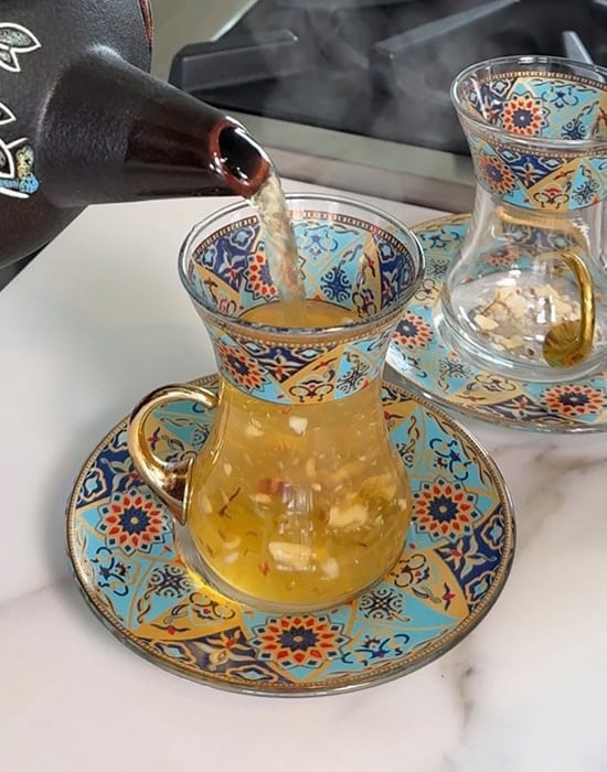 a kettle pouring hot tea into a blue color tea cup
