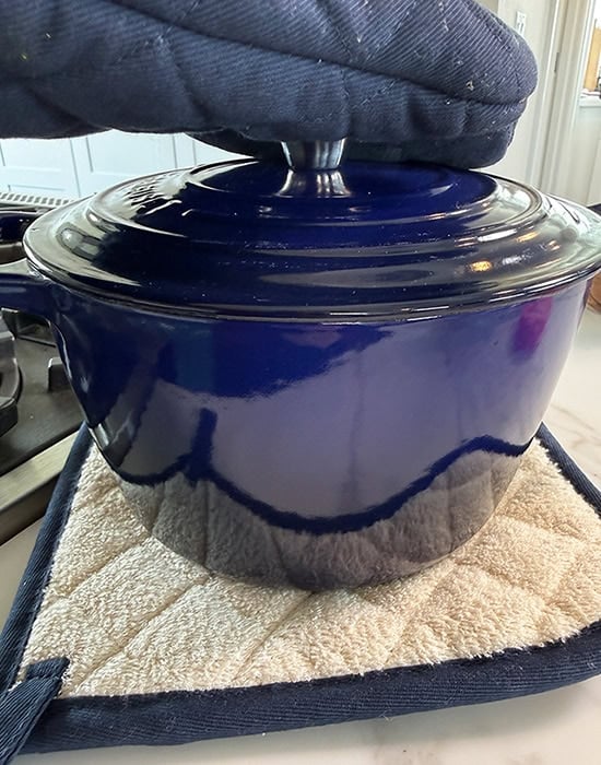 hand covering a blue water pot with a lid using gloves