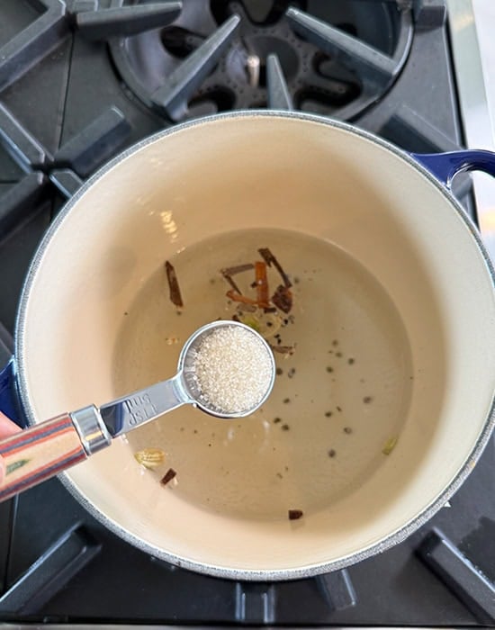 sugar being added to a pot of water with spices