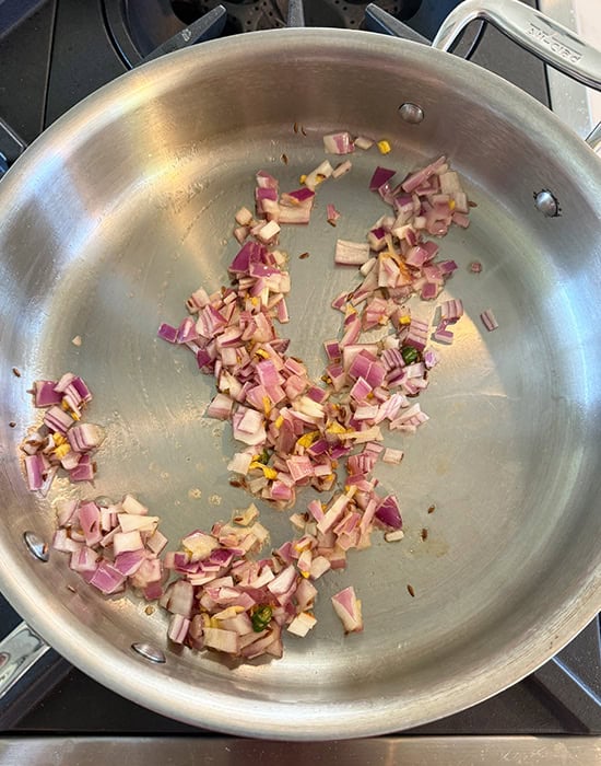chopped onions being sauteed in a steel pan
