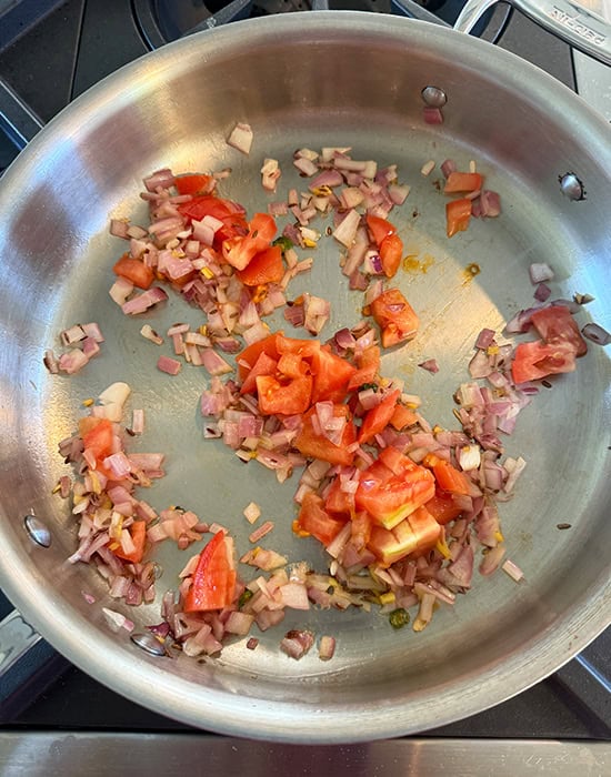 chopped onions with tomatoes in a steel pan