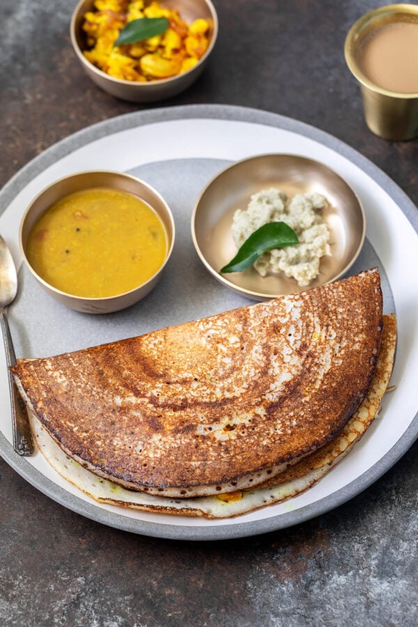 paneer dosa in a plate with 2 bowls filled with sambar and coconut chutney