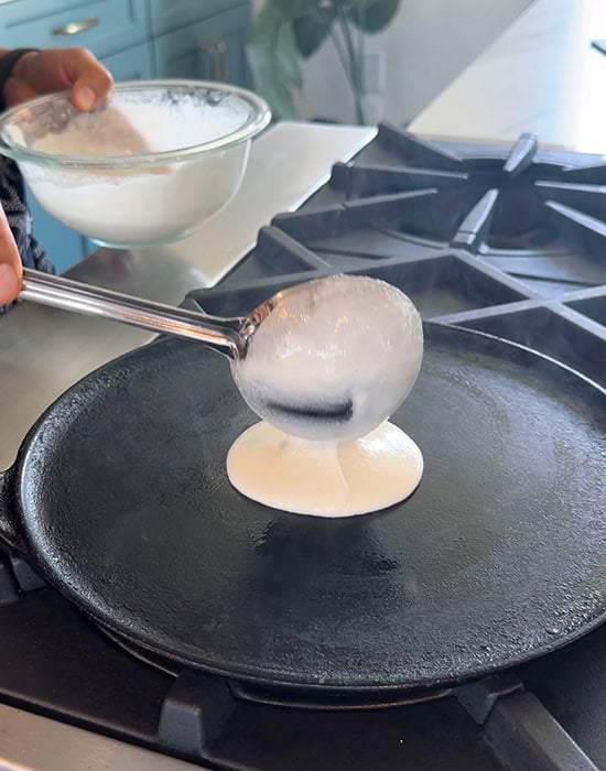 pouring dosa batter on a tawa with a ladle