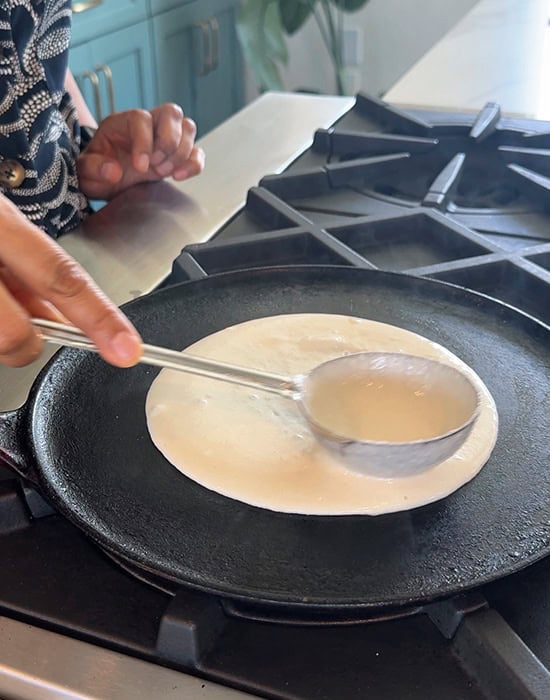 spreading dosa batter on a tawa using a ladle