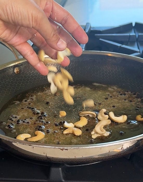 adding cashews to pan with whole spices