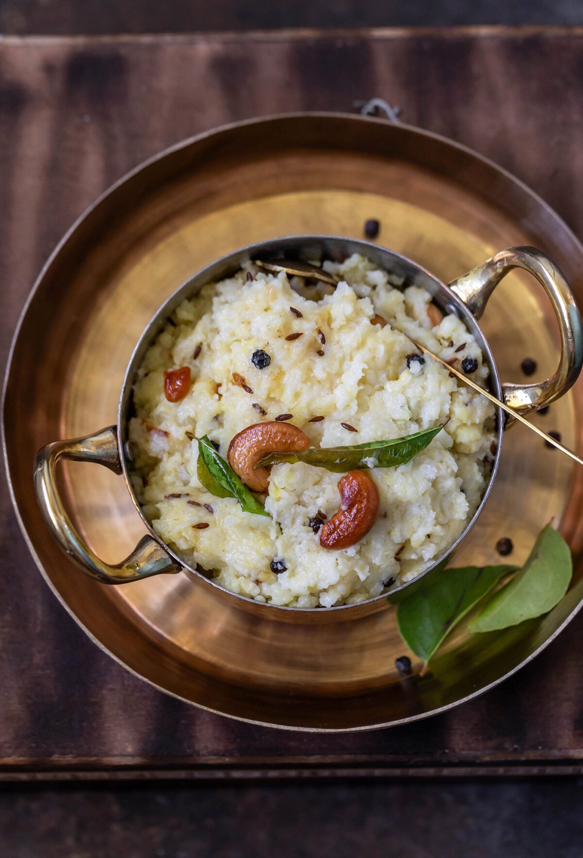 overhead shot of ven pongal served in a copper bowl with handles