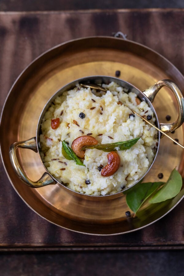 overhead shot of ven pongal served in a copper bowl with handles