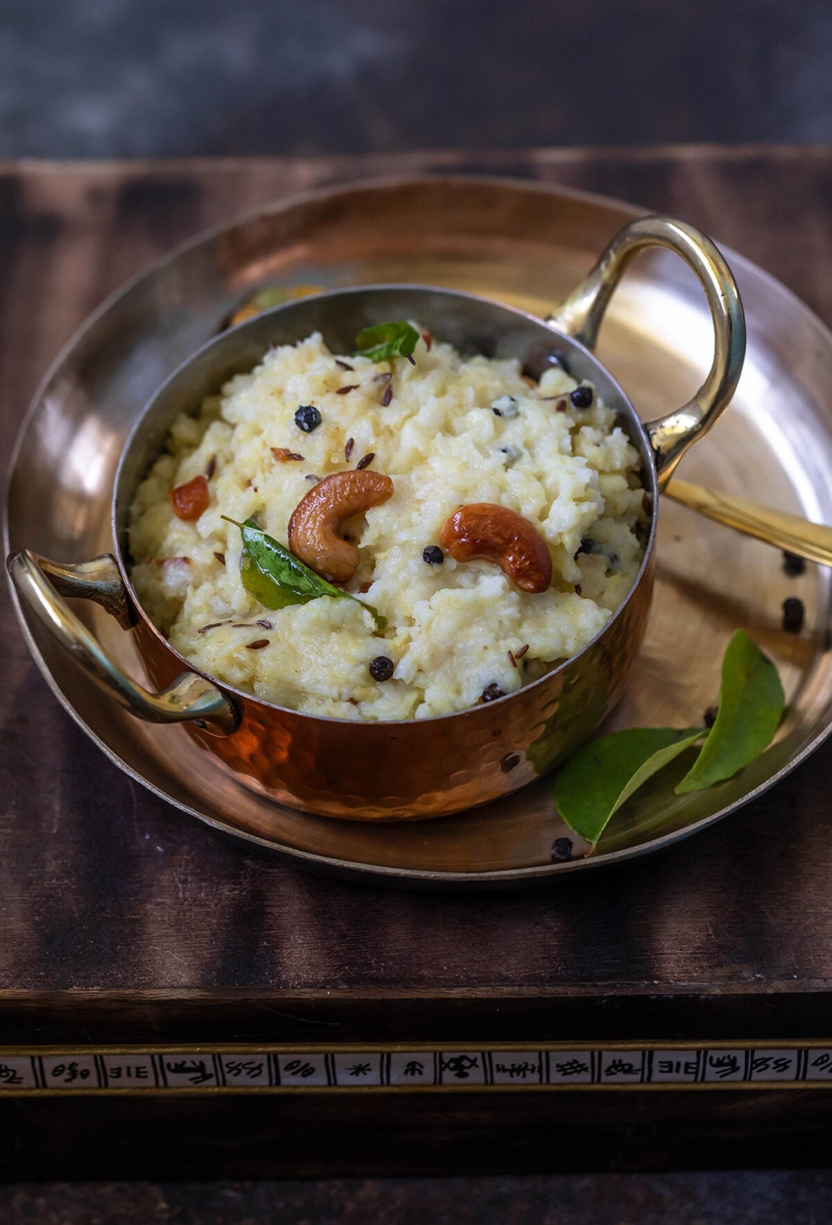 ven pongal served in a copper kadai garnished with curry leaves and cashews