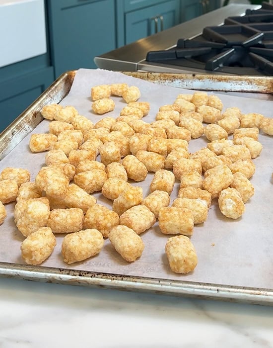 frozen tater tots arranged on a baking sheet lined with parchment paper