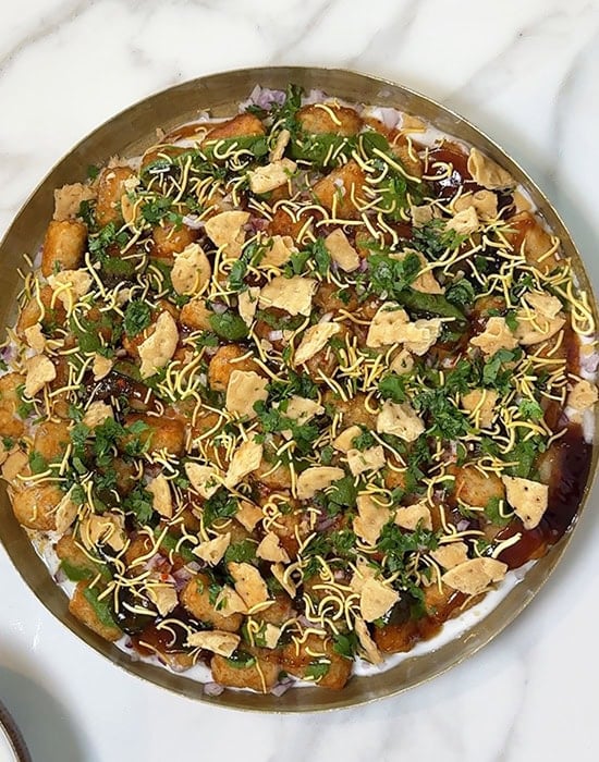 overhead shot of tater tots topped with chutney and papdi arranged in a plate