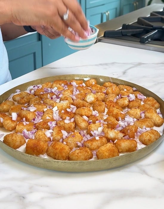 chopped onions sprinkled over tater tots in a plate