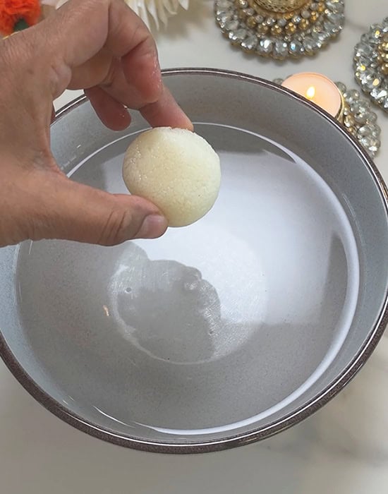 hand holding a white rasgulla to drop it in water