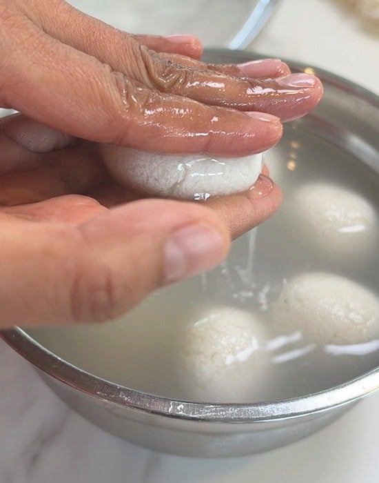 hands squeezing water out of a rasgulla